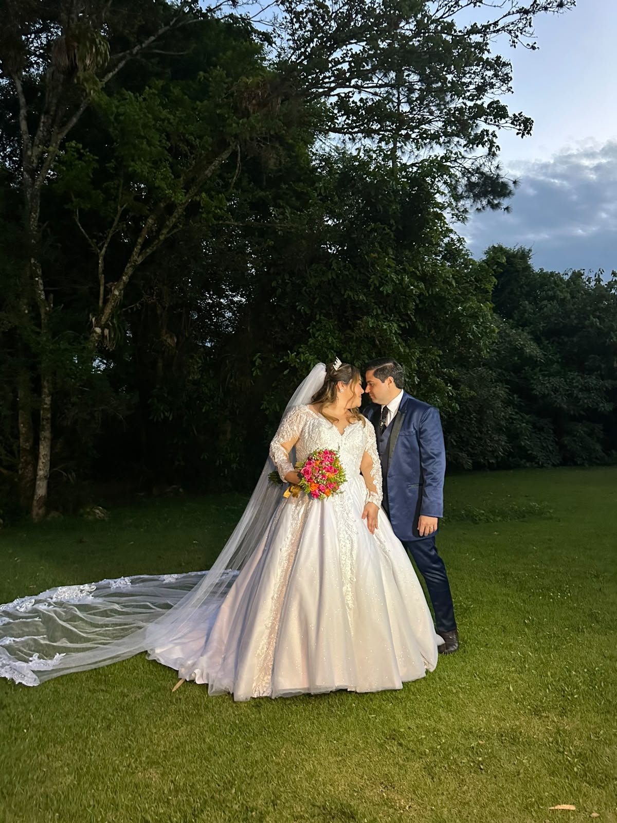 Rayssa e Caio no jardim no dia do casamento, com o vestido e o véu inteiros